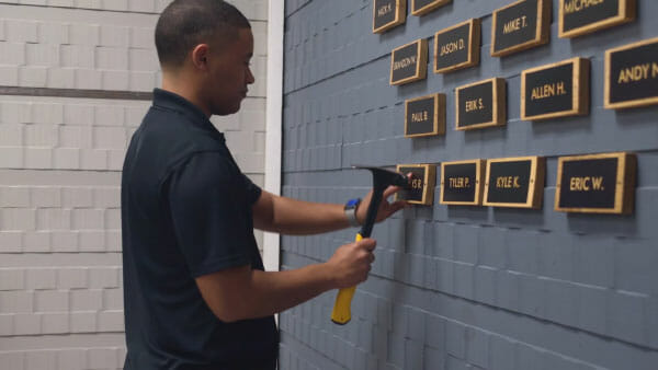 man using hammer to install plaque marking one year of sobriety on a wall at guiding light mission
